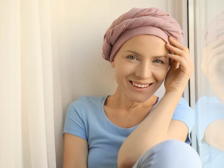 Begleittherapie mit PANACEO – Unterstützung und neue Lebensqualität während der Chemotherapie Eine lächelnde Frau mit Kopftuch sitzt am Fenster. Das Bild steht für Hoffnung, Lebensfreude und Unterstützung während der Chemotherapie mit PANACEO