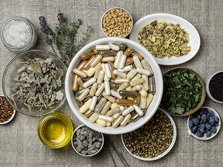 Natürliche Nahrungsergänzung mit Vitaminen und Mineralstoffen – Green Health von PANACEO Eine Auswahl an Nahrungsergänzungskapseln in einer Schale, umgeben von frischen Kräutern, Samen und natürlichen Zutaten. Symbol für natürliche Vitamine und Mineralstoffe mit PANACEO Green Health.